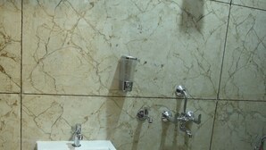 A bathroom with a marble floor, a white sink, a handheld showerhead, and a handheld shower attachment. - Hotel Kumar Continental (Jhusi)