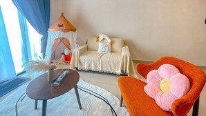 A cozy room with a bed, a small table, a chair with a large flower pillow, a tent, and a wall with a sign.