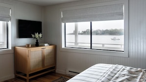 Een slaapkamer met een groot raam, een houten kast, een bed met streepjesbeddengoed en een zwart plafondlamp.