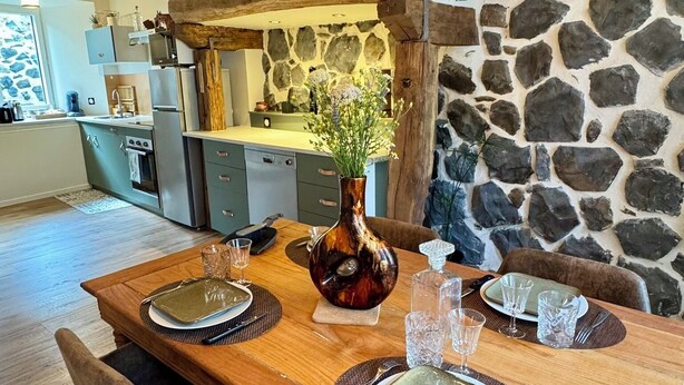 A rustic dining area with a wooden table set for four, stone walls, and hanging pendant lights. - House in the shadow of the bell tower (Laguiole)