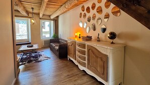 A cozy living room with a wooden ceiling, a large window, a leather sofa, a white cabinet, and a wall decorated with oval mirrors. - House in the shadow of the bell tower (Laguiole)