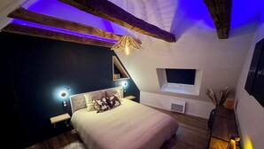A bedroom with a bed, wooden beams, a window, and a ceiling light fixture. - House in the shadow of the bell tower (Laguiole)