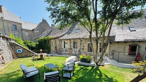 A courtyard with stone buildings, outdoor seating, and a small garden area. - House in the shadow of the bell tower (Laguiole)