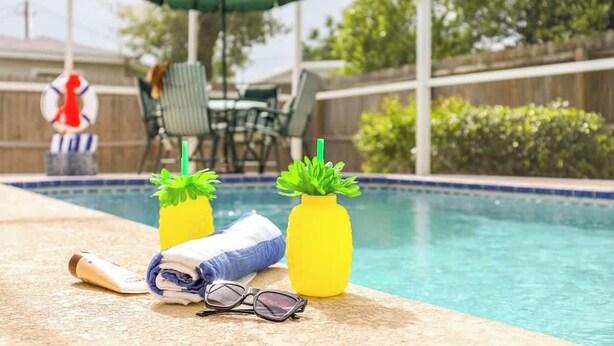 Zona junto a la piscina con una silla, una toalla, gafas de sol y dos macetas amarillas con plantas verdes.