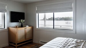 Ein Schlafzimmer mit großem Fenster, einem Holzkasten, einem Bett mit gestreifter Bettdecke und einer schwarzen Deckenleuchte.