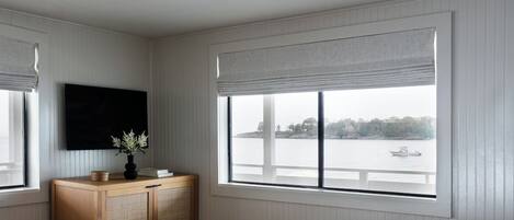 A bedroom with a large window, a wooden cabinet, a bed with a striped bedspread, and a black ceiling light.