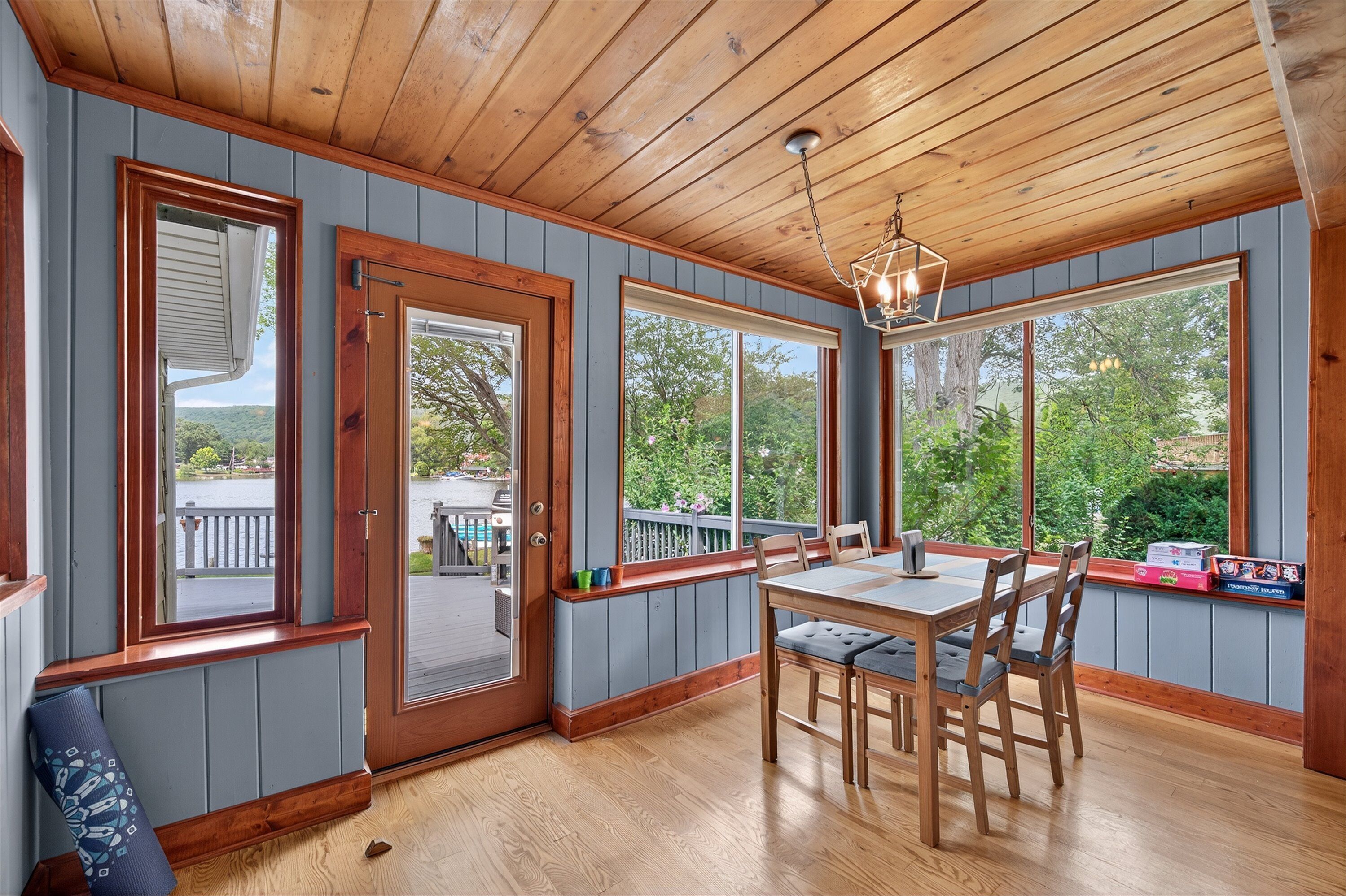 A dining area with a wooden table and chairs, large windows, and a view of the outdoors.