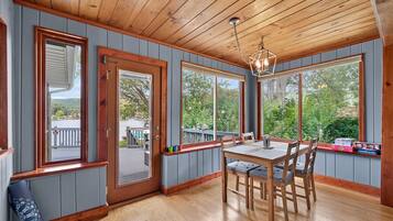 A dining area with a wooden table and chairs, large windows, and a view of the outdoors.