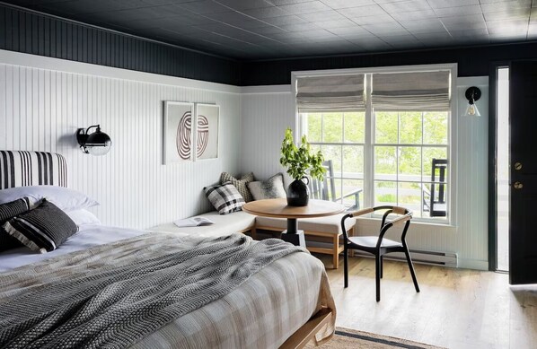 A bedroom with a bed, a round table, a chair, a potted plant, and a window with a view of greenery. - Quaint Oceanfront Room Perfect for Relaxing After Adventurous Days | with Pool (Boothbay)