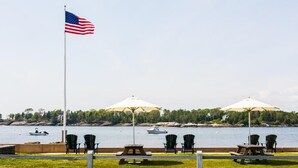 Ein Fahnenmast mit einer amerikanischen Flagge, Sitzgelegenheiten im Freien mit Sonnenschirmen und Blick auf einen See mit Booten.