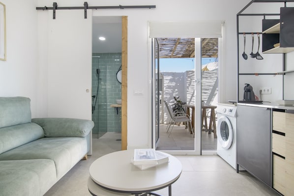 A modern kitchen with a washing machine, a dining area with a table and chairs, and a sofa.