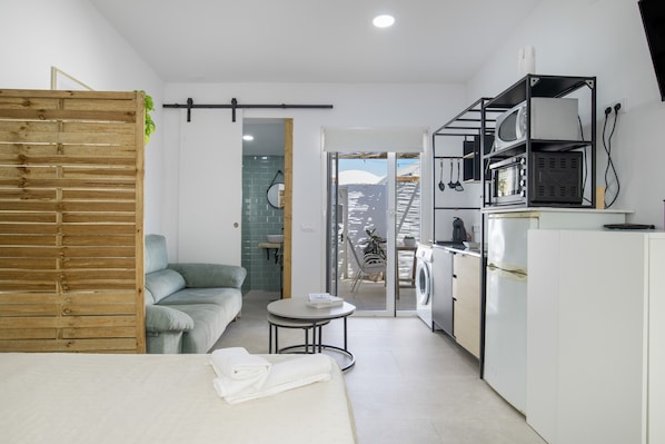 Een knus woongedeelte met een bed, een slaapbank, een klein rond tafeltje, een wasmachine en een kitchenette.