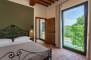 A bedroom with a bed, a wooden door, and a balcony with a view of greenery and a pool. - Villa Fiorda by MMega (Città di Castello)