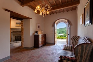 A room with a fireplace, a wooden dresser, a sofa, and an arched doorway leading to a garden.
