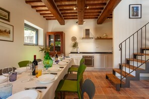 A dining area with a long table set for four, a kitchen in the background, and a staircase. - Villa Fiorda by MMega (Città di Castello)