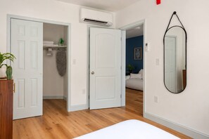 A bedroom with a bed, a wardrobe, a mirror, and a hallway leading to a living area.
