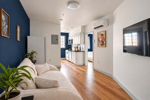 Un salon moderne avec un canapé, un téléviseur à écran plat et une cuisine en arrière-plan.