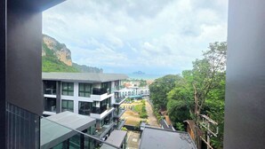 A modern building with multiple floors, large windows, and a view of a coastal area with greenery and a cliff. - Room-a304 - 1 Bedroom Condo With Sea Vie (Krabi)