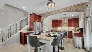 A modern kitchen with a central island, bar stools, stainless steel appliances, and a staircase with a railing. - 4BR w pool, fire pit, game room (Queen Creek)