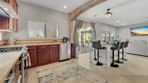 A modern kitchen with a gas stove, a dishwasher, and a dining area with a table and chairs. - 4BR w pool, fire pit, game room (Queen Creek)
