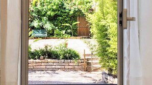 Una ventana con vista a un jardín, un banco y un muro de ladrillo.