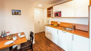 A compact kitchen with white cabinets, a wooden countertop, a red microwave, and a sink.
