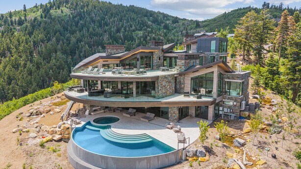 Una casa moderna de varios pisos con una piscina circular, rodeada por un paisaje natural.