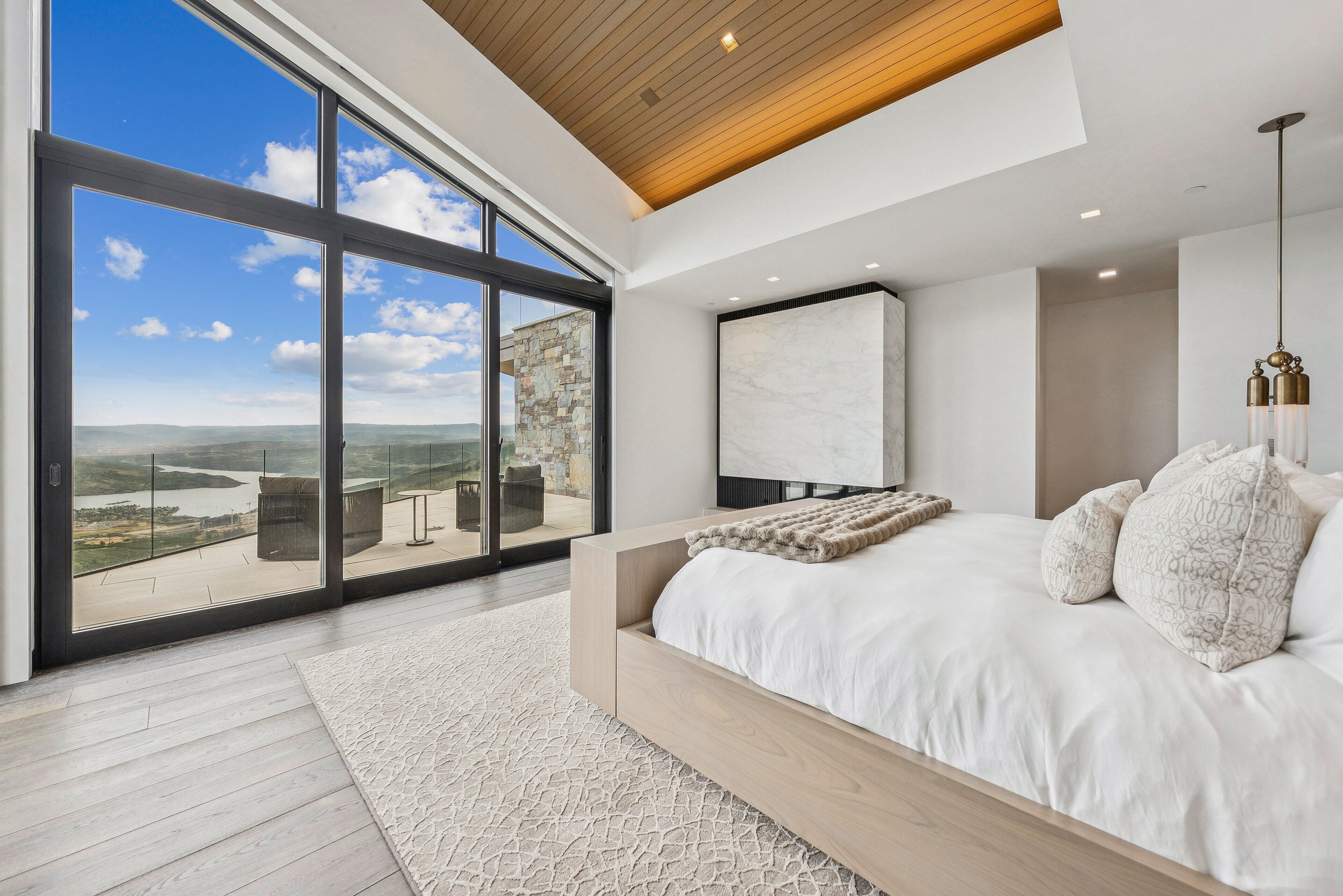 A bedroom with a large bed, a view of a river, and a stone wall.