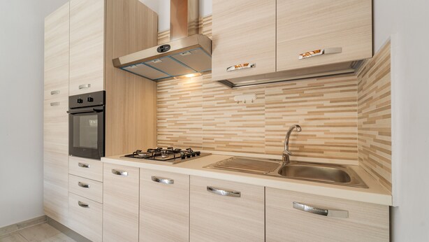 A modern kitchen with a built-in oven, gas stove, stainless steel sink, and wooden cabinetry. - Apartment 'Maria Rosa' with Private Terrace, Wi-Fi and Air Conditioning (Teulada)