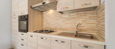 Een koelkast, een oven, een kookplaat, kookgerei, borden en bestek