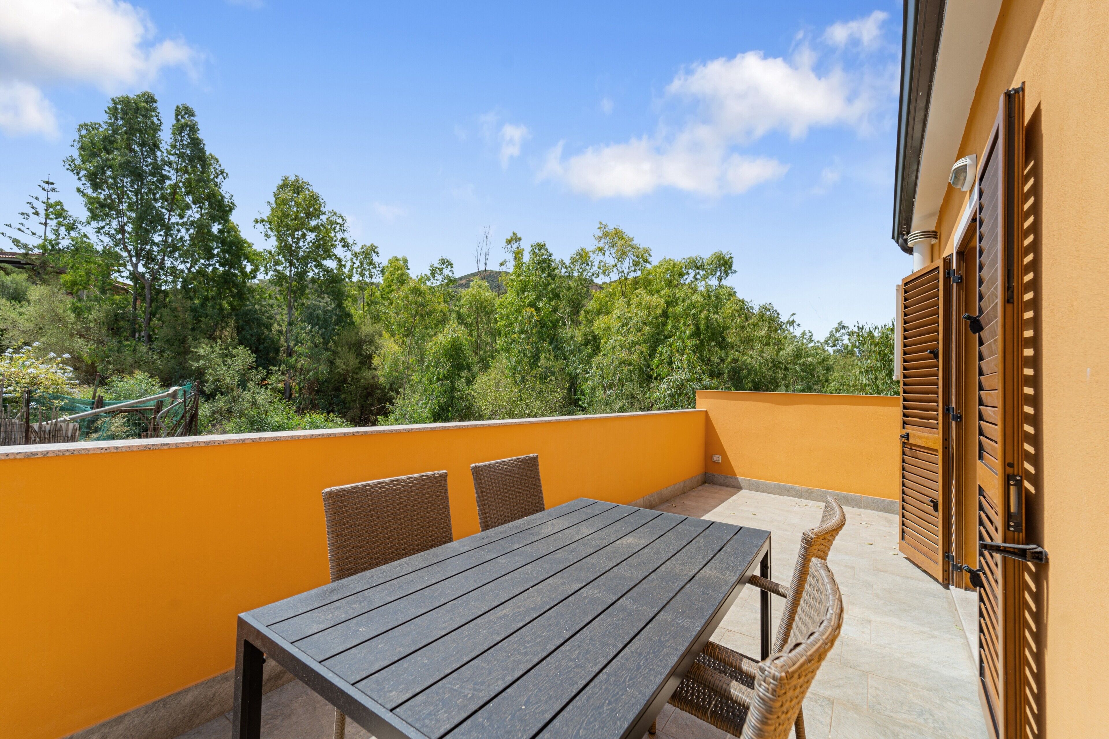 Un balcon avec une table en bois et des chaises en osier, donnant sur un paysage verdoyant et luxuriant.