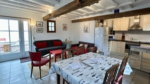 A spacious living area with a dining table, red chairs, a sofa, and a kitchen area with cabinets and appliances. - 🏡 Chez Tata - Authentic vacation home in the heart of Le Crotoy (Le Crotoy)