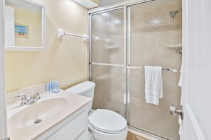 A bathroom with a sink, toilet, and glass shower enclosure. - Beachfront Comfort w/ Pool, Balcony & Steps to Flagler Avenue (New Smyrna Beach)