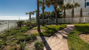 A coastal hotel with a paved walkway, palm trees, and a view of the ocean. - Beachfront Comfort w/ Pool, Balcony & Steps to Flagler Avenue (New Smyrna Beach)