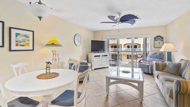 A living room with a white table, chairs, a glass coffee table, a sofa, a TV, and a ceiling fan. - Beachfront Comfort w/ Pool, Balcony & Steps to Flagler Avenue (New Smyrna Beach)