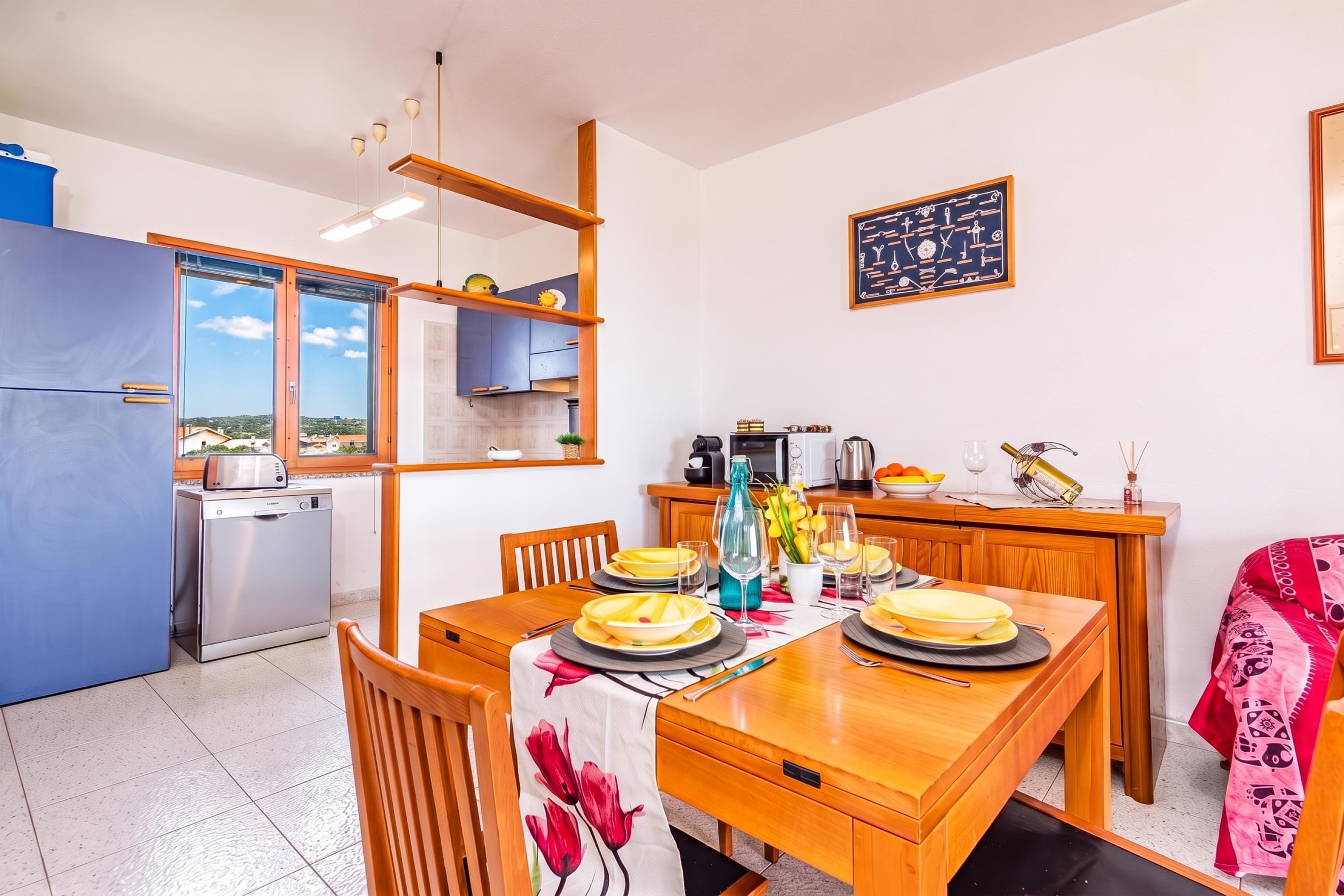 A modern kitchen with a dining area, a view through the window, and a chalkboard with drawings.