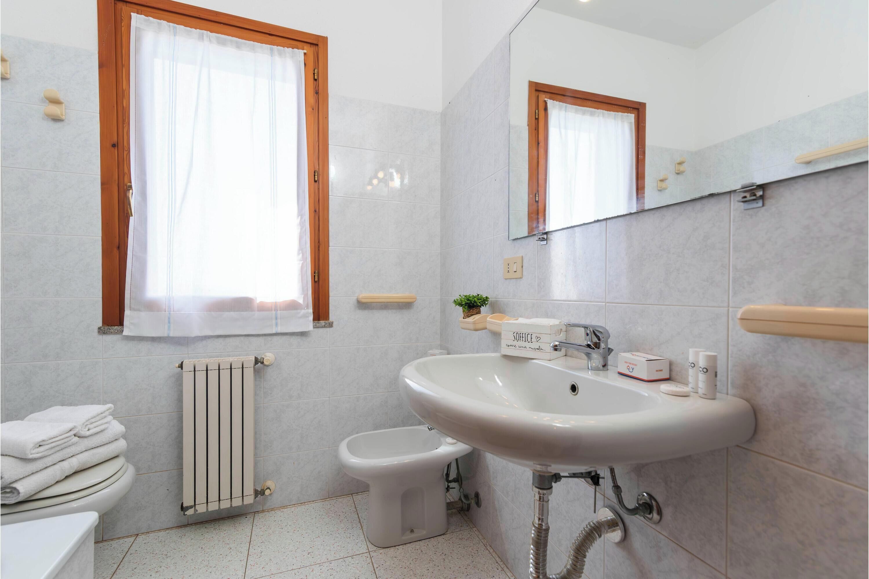 Une salle de bain avec un lavabo blanc, des toilettes, un bidet, un porte-serviettes et une fenêtre avec des rideaux.