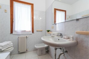 Un baño con lavamanos blanco, inodoro, bidé, toallero y ventana con cortinas.