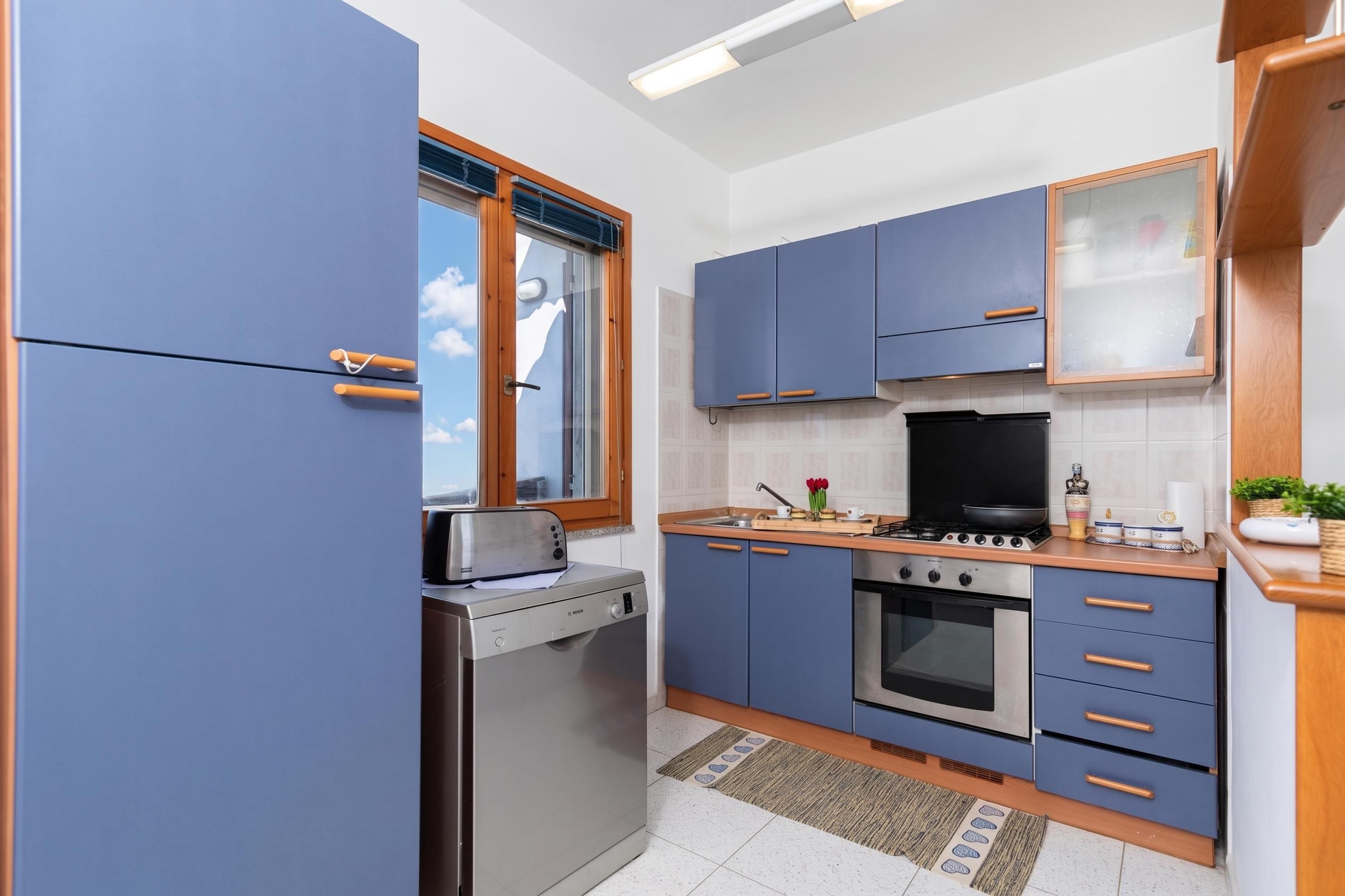 Una cocina compacta con armarios azules, horno integrado, estufa y tostadora.