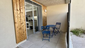 Un pati amb taula i cadires, una porta corredissa de vidre que dona a una cuina, i una petita zona de jardí.