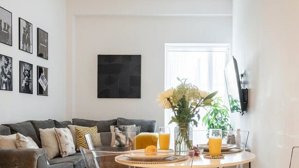 Una sala de estar moderna con un sofá gris, una mesa de comedor redonda con sillas y un televisor montado en la pared.