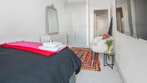 Un dormitorio con cama, cómoda, espejo, televisor y una alfombra colorida.