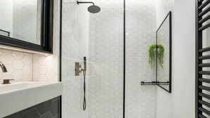 Un baño moderno con cabina de ducha de vidrio, salpicadero de azulejos hexagonales blancos y un espejo con marco negro sobre el lavamanos.