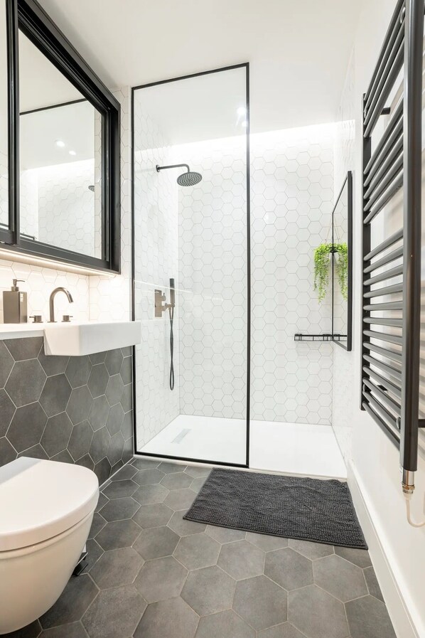 A modern bathroom with a glass-enclosed shower, a white sink, and a toilet.