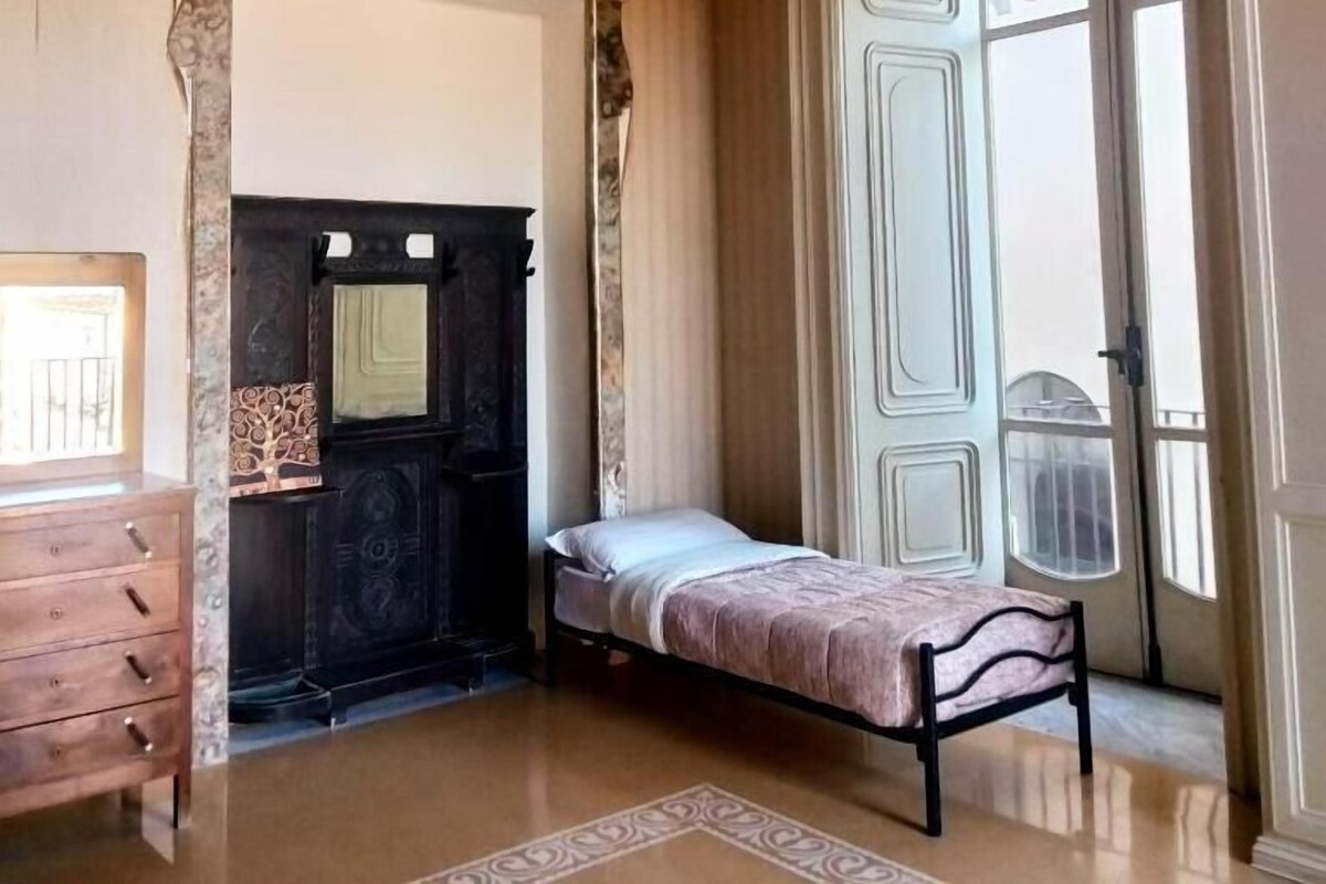 Um quarto com uma cama, cômoda, lareira e uma janela grande.