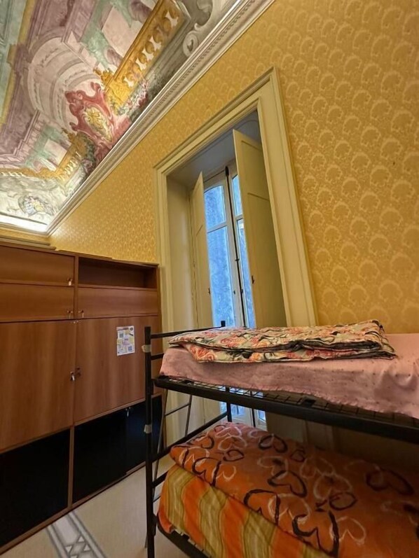 A bunk bed with a patterned blanket, a wooden wardrobe, and a decorative ceiling. - Salerno Experience HOSTEL (Salerno)