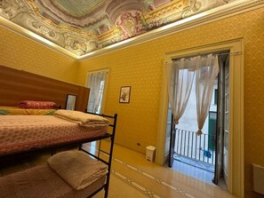Una habitación con dos camas, un balcón con barandilla y un techo decorativo.