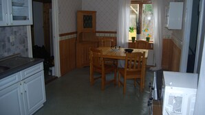 A kitchen with a dining table, chairs, wooden cabinets, and a window with curtains. - Malaskog nature reserve Baden (Malaskog)
