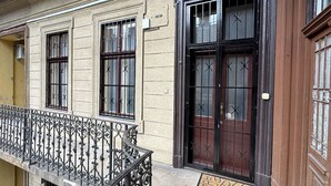 Fachada de edificio con una reja metálica negra, felpudo y un ventanal con vidrios protegidos.