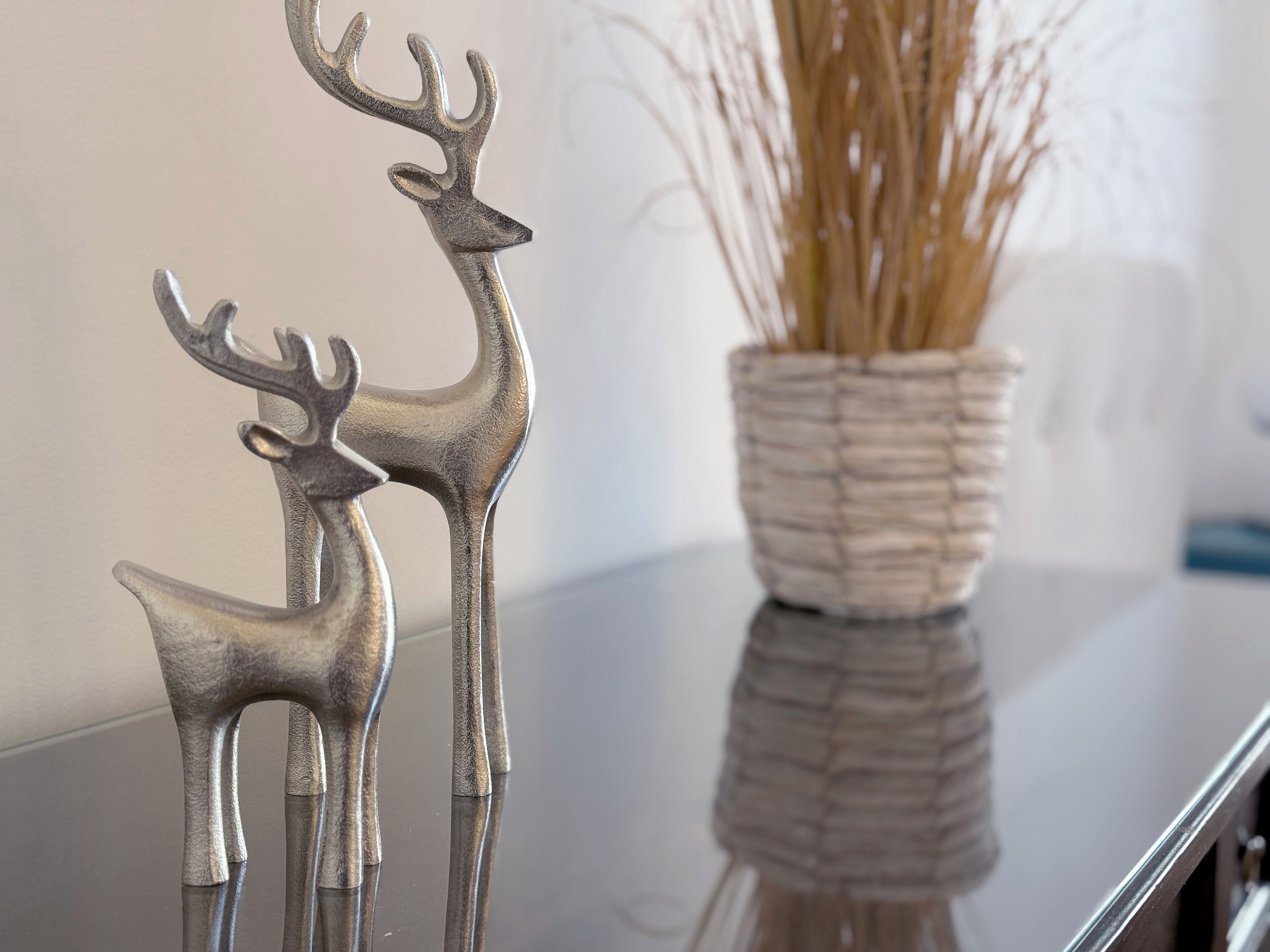 Two metallic deer-shaped wall decor items on a reflective surface, with a woven basket containing dried plants in the background.